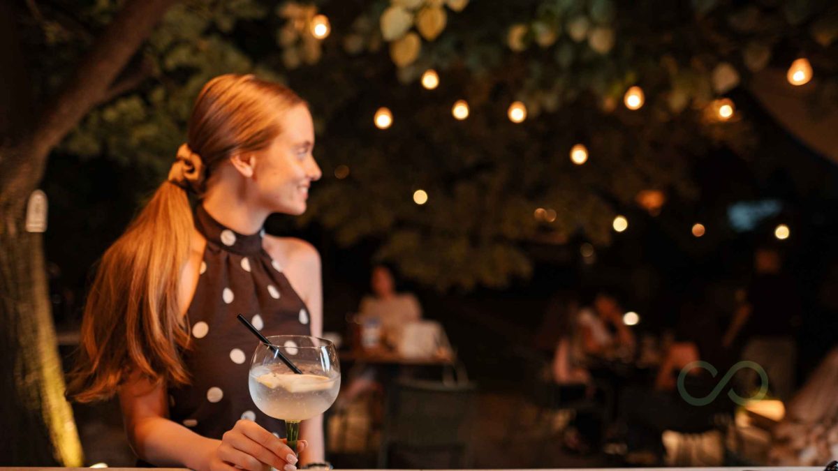 Woman enjoying a cocktail at an outdoor bar with warm ambient lighting Ice and energy: invisible but expensive Green Loop